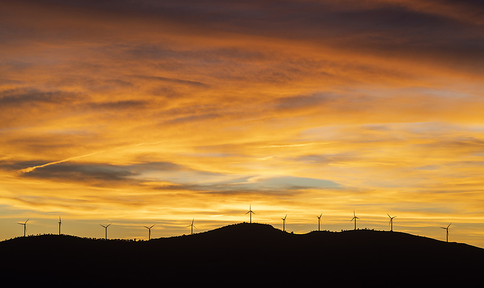 Moody sky over silhouettes of wind farm turbines at sunset