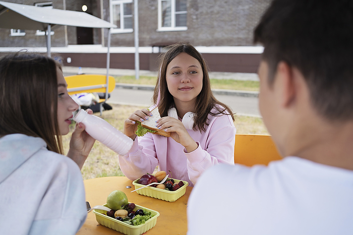 Thoughtful girl holding sandwich sitting with friends at table in schoolyard