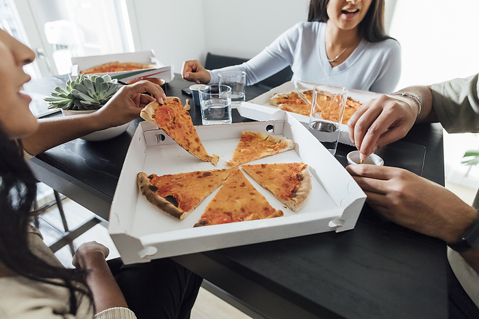 Hands of women and man by pizza box on table at home