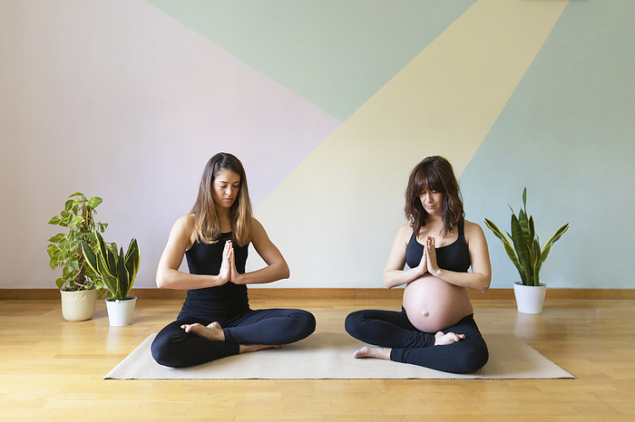 Maternity yoga class Pregnant woman meditating with yoga instructor sitting in front of wall at studio
