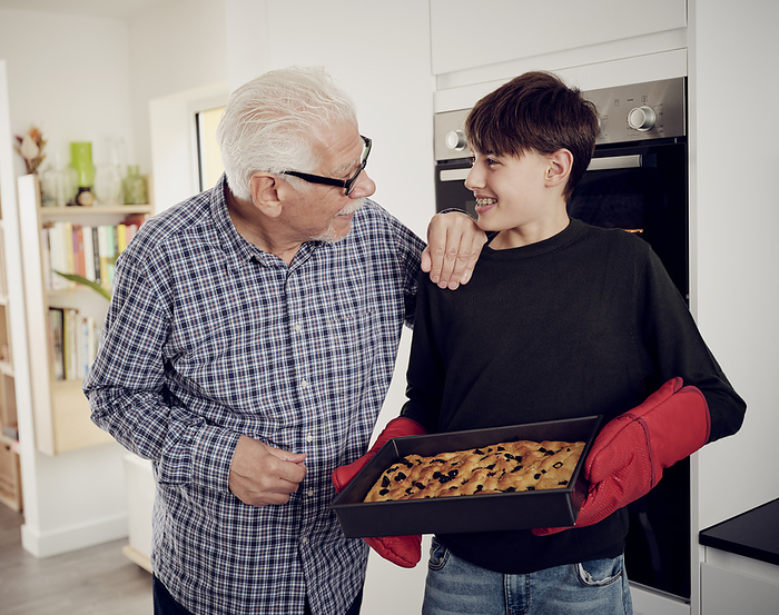 Grandfather and grandson holding baking tray with fresh focaccia bread in the kitchen