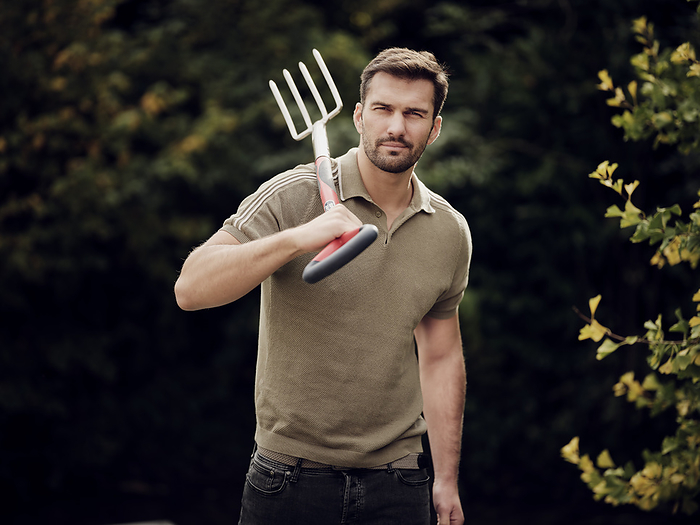 Man with garden fork on shoulders standing in his garden