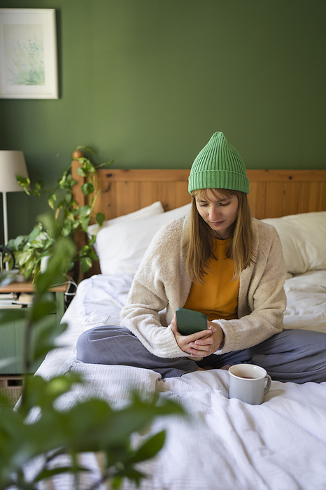 Woman wearing knit hat sitting on bed at home