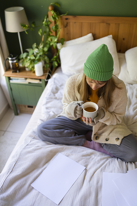Woman sitting with tea cup on bed at home