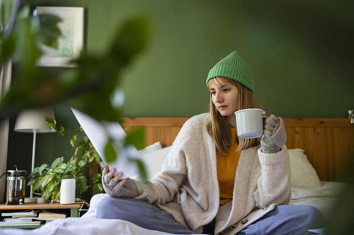 Woman examining financial bills sitting on bed at home