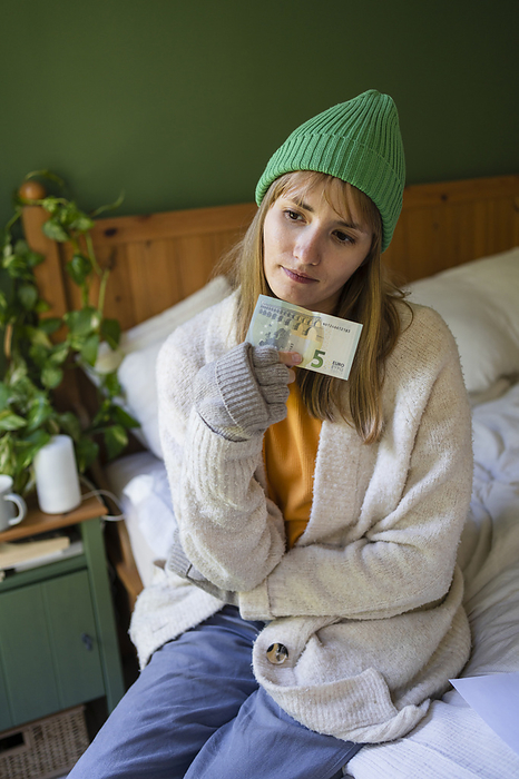Thoughtful woman with paper currency sitting on bed at home