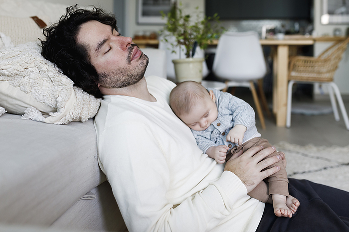 Father and baby boy sleeping together in living room at home