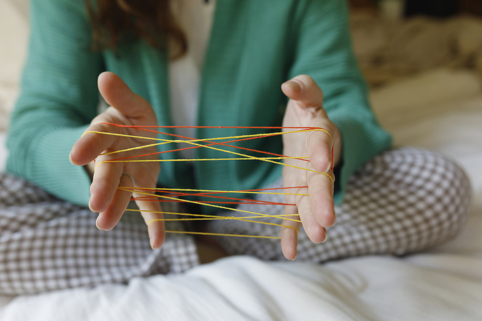 Hands of woman playing cats cradle game at home