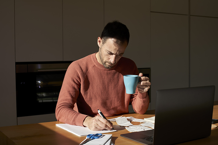 Man with coffee cup writing on paper at desk