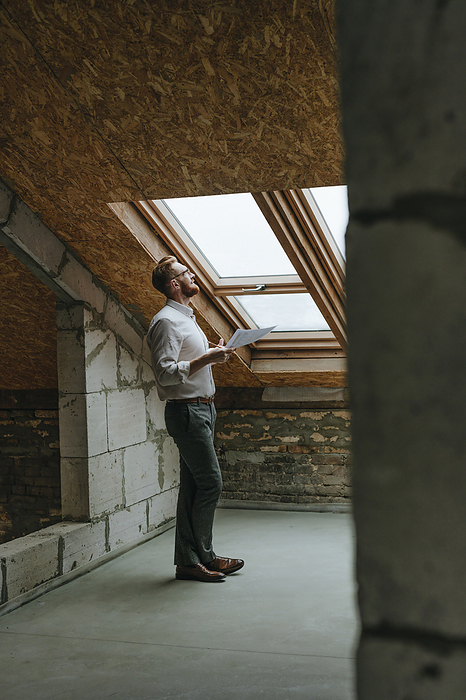 Architect with blueprint looking through window at construction site