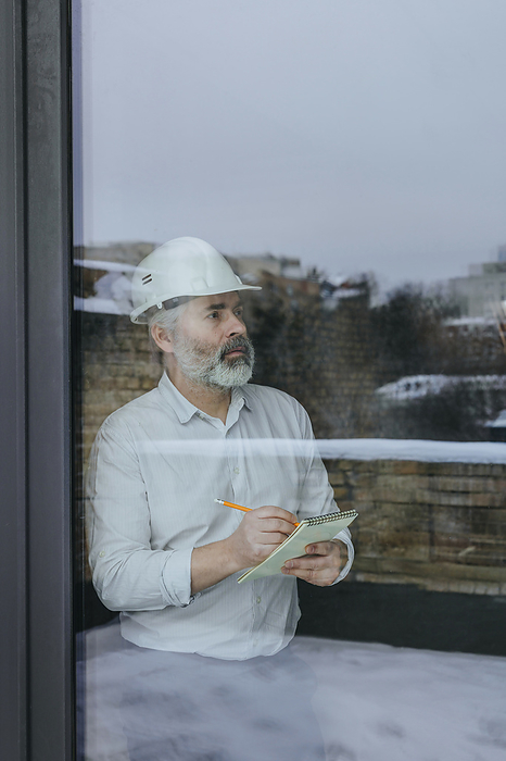 Architect with diary making notes near window seen through glass