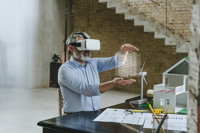 Businessman wearing VR glasses gesturing with model house on desk at construction site