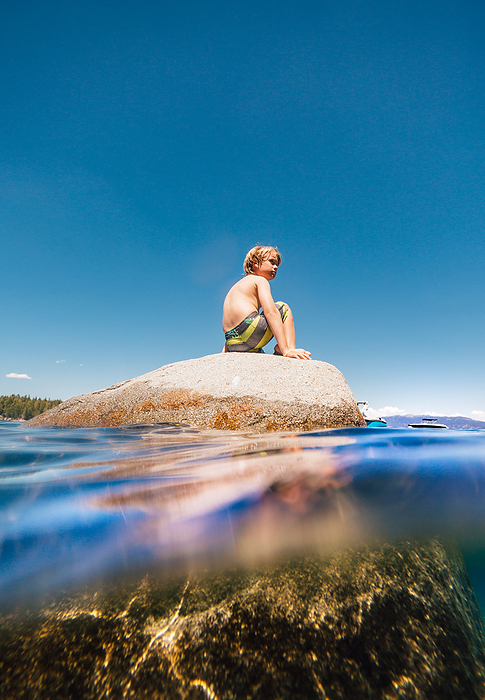 USA, California, Boy sitting on boulder in Lake Tahoe