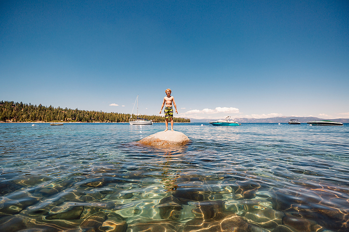 USA, California, Boy standing on boulder in Lake Tahoe