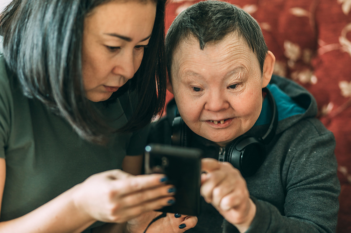 elderly woman with Down syndrome, asian assistant helps  to use phone