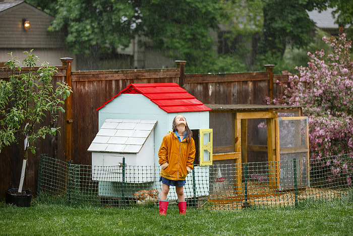 A happy girl stands in rain by chicken coop face turned up