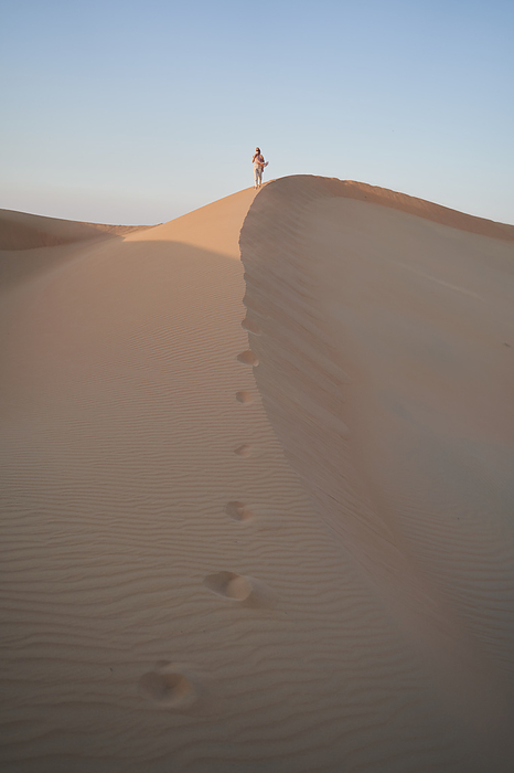 Spectacular vertical shot with a woman walking by sand dine in desert.