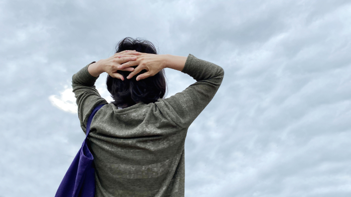 Woman holding her head and looking up at the cloudy sky