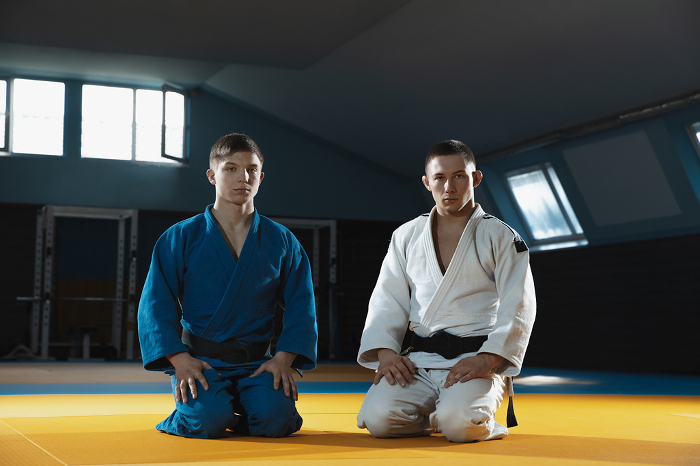 Two young judo fighters in kimono posing comfident in the gym, strong and healthy Two young judo caucasian fighters in white and blue kimono with black belts posing confident in the gym, strong and healthy. Practicing martial arts fighting skills. Overcoming, reaching target.