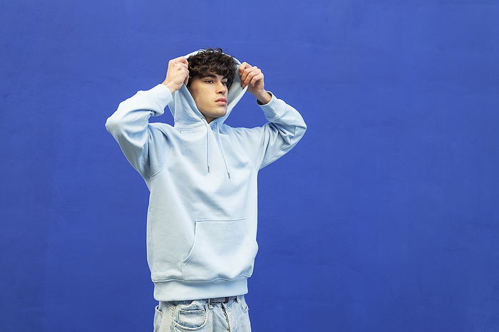 Young man wearing hooded shirt in front of blue wall