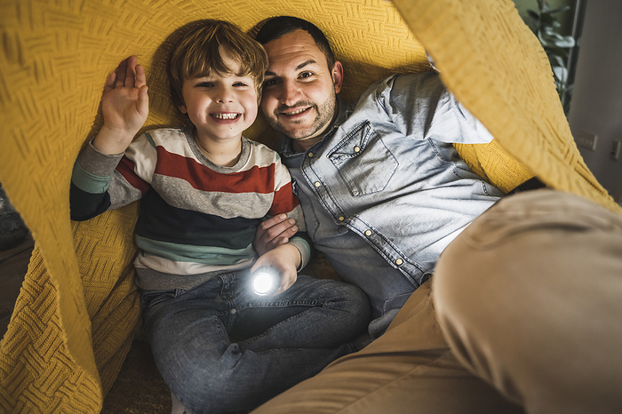 Happy father and son with torch under yellow blanket