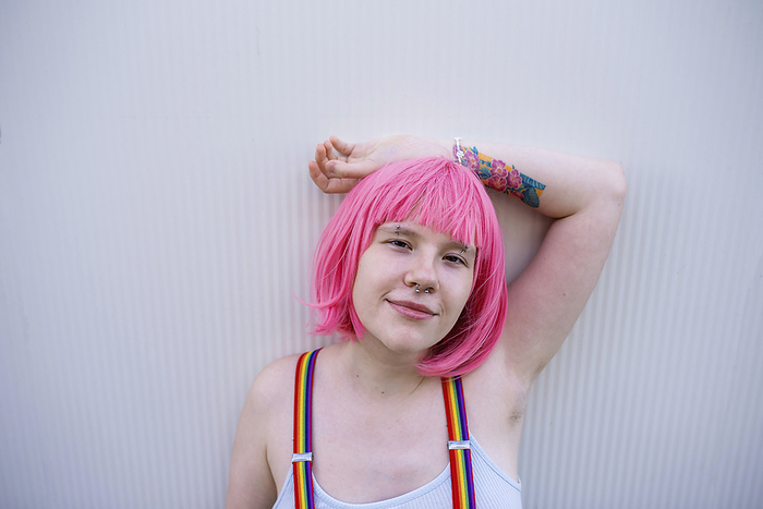 Smiling non-binary person wearing pink wig in front of gray wall