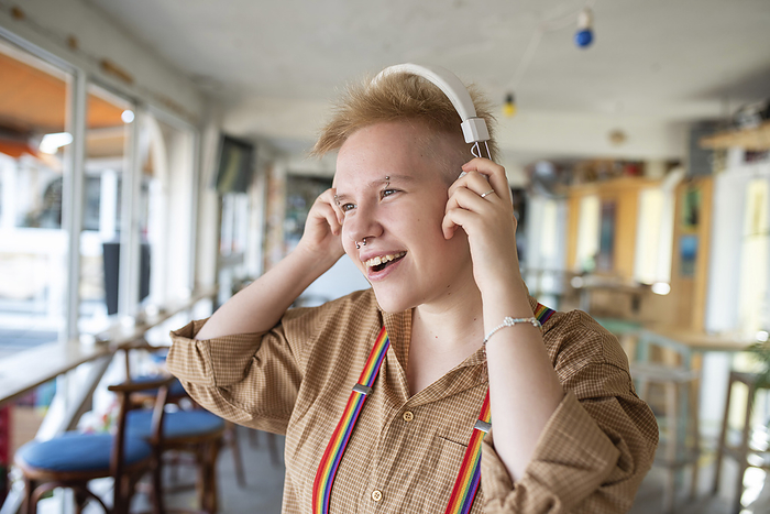 Non-binary person wearing headphones listening to music in cafe
