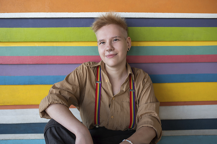 Smiling non-binary person sitting in front of multi colored wall