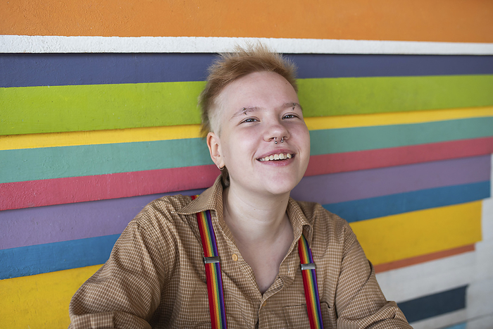 Happy non-binary person in front of multi colored wall