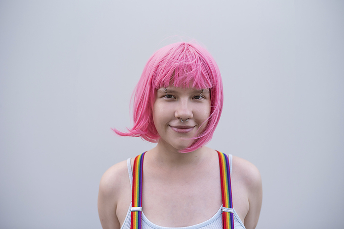 Smiling non-binary person wearing pink wig in front of wall