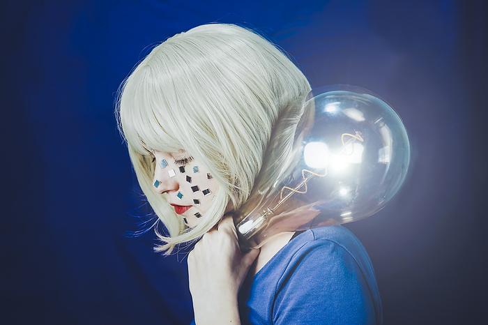 Blond woman holding illuminated large bulb against blue background