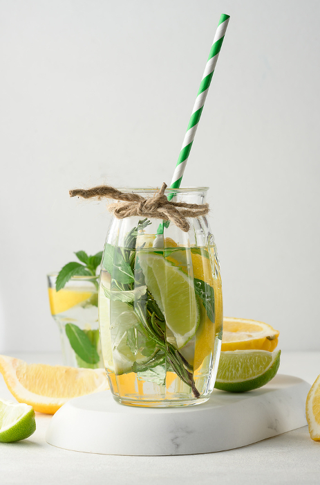 Lemonade in a transparent glass with lemon, lime, rosemary sprigs and mint leaves on a white background Lemonade in a transparent glass with lemon, lime, rosemary sprigs and mint leaves on a white background