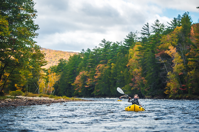 Woman smiling while paddling river in packraft in fall foliage Woman smiling, laughing while paddling river in packraft