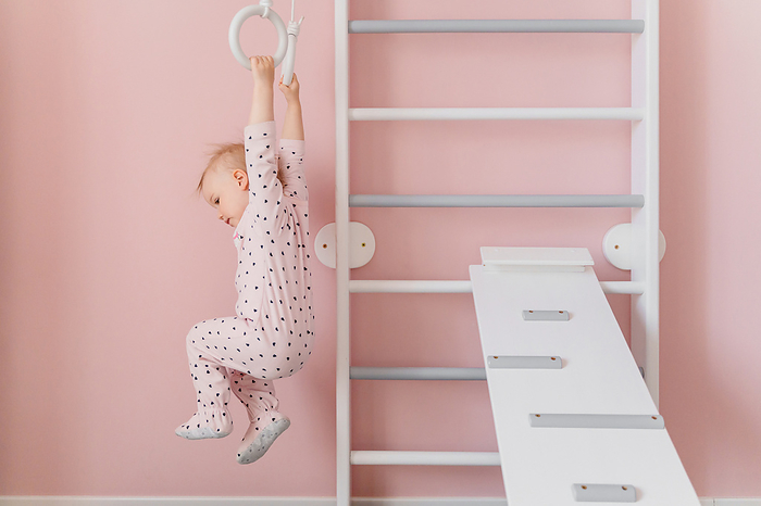 A Caucasian girl in soft pink pajamas does sport at gymnastic rings
