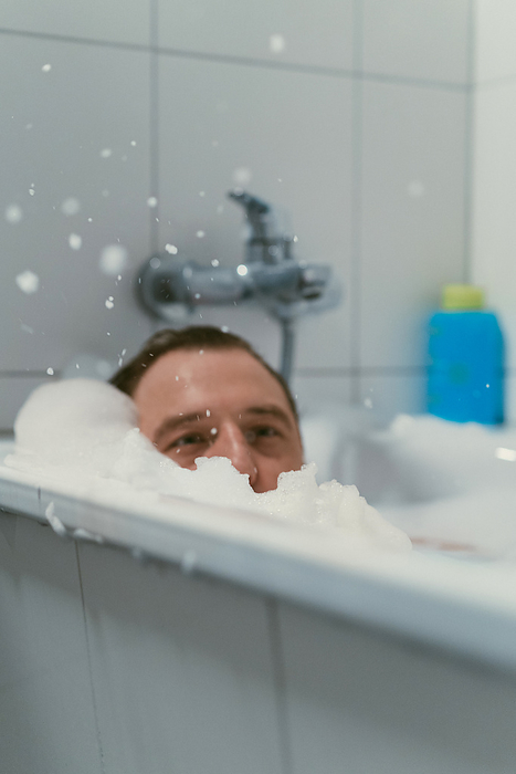 Young tattooed man laying in bubble bath.