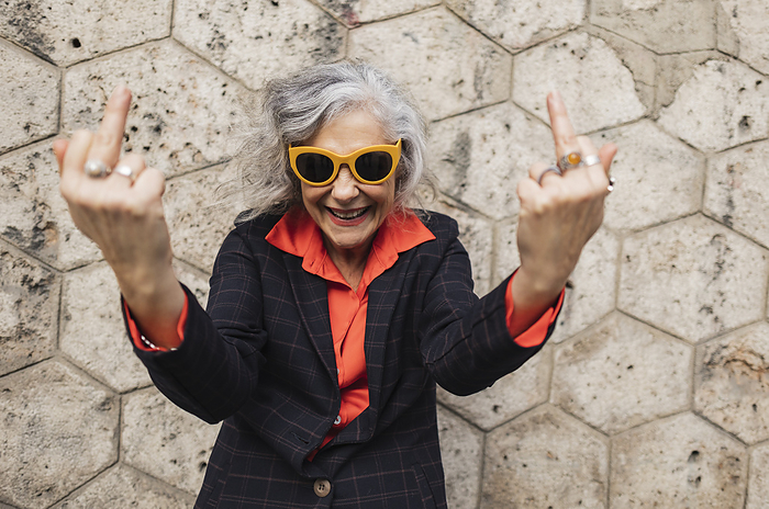 Carefree businesswoman showing obscene gesture in front of wall