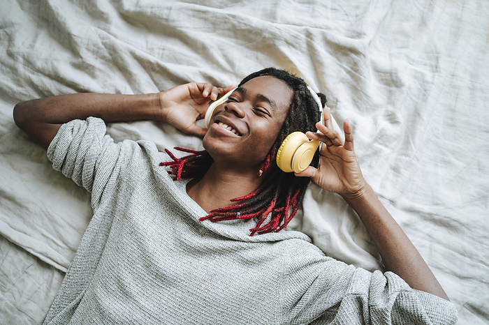 Happy man wearing headphones listening to music lying on bed at home
