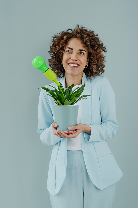 Thoughtful woman standing with green light bulb in potted plant against blue background