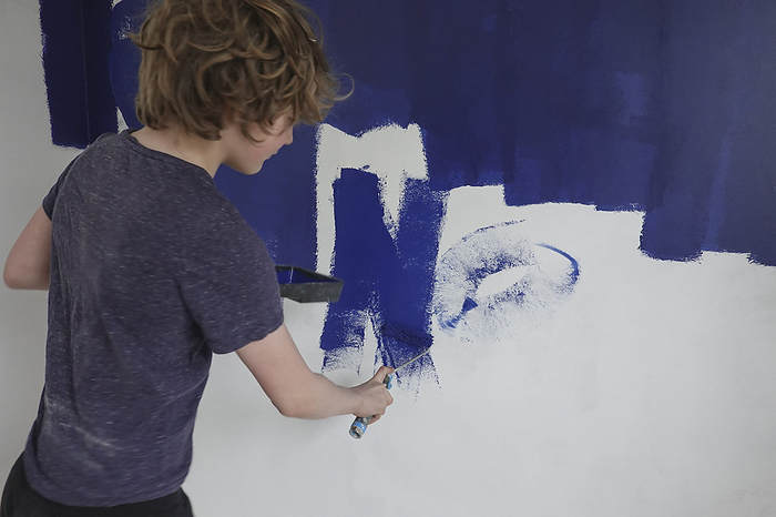Boy painting wall with blue paint
