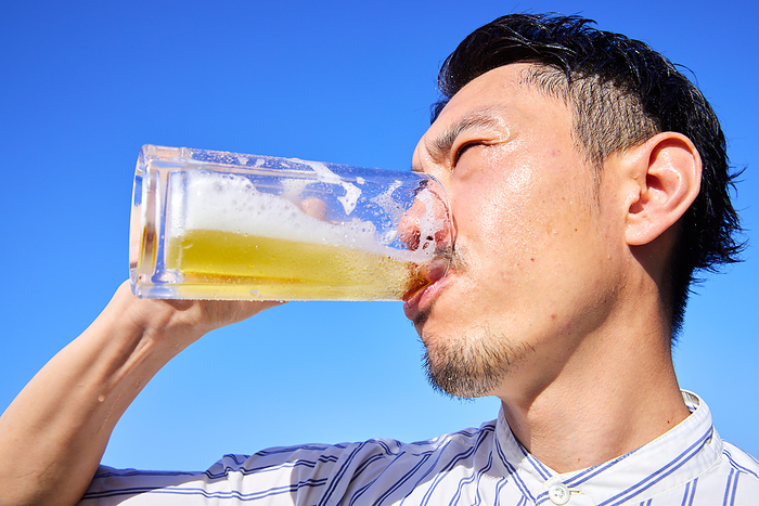 Young Japanese man drinking beer under blue sky