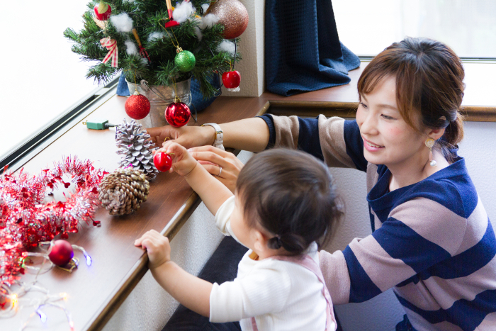 A mother and a one-year-old girl decorating a Christmas tree.
