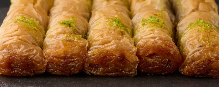 Pieces of baked baklava in honey and sprinkled with pistachios on a black board, close up Pieces of baked baklava in honey and sprinkled with pistachios on a black board, close up
