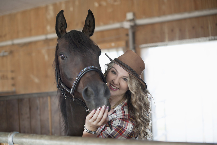 horsewoman is stroking her horse in the stable,horse riding center,liberty,freetime,love to animals, Portrait of a young woman stroking her brown horse in barn and smiling, Bavaria, Germany