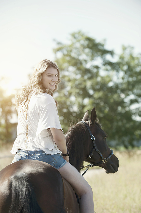 horse woman is riding and smiles over her shoulder,horse riding center,liberty,freetime,love to animals, Young woman riding a horse in farm looking over shoulder and smiling, Bavaria, Germany