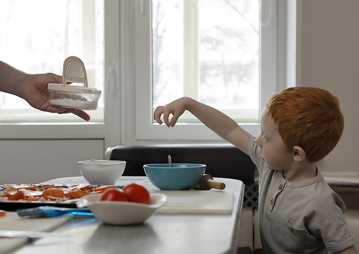 Child cooks with dad. The kid pours salt into a plate.