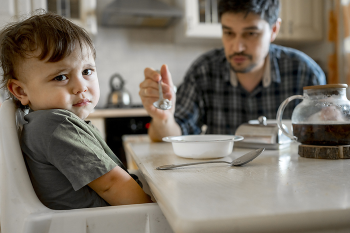 Son refusing to eat food being fed by father at home