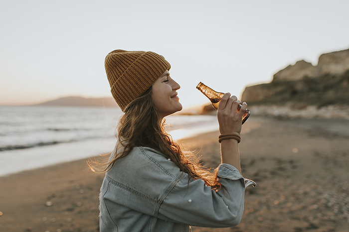 Smiling woman with beer bottle standing at beach