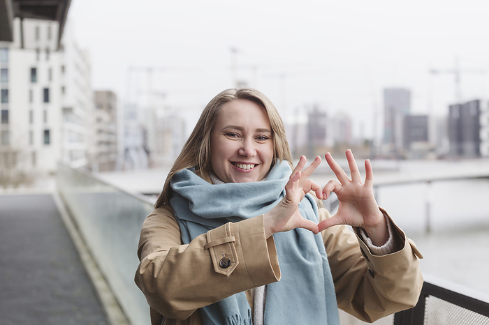 Happy woman making heart gesture by railing