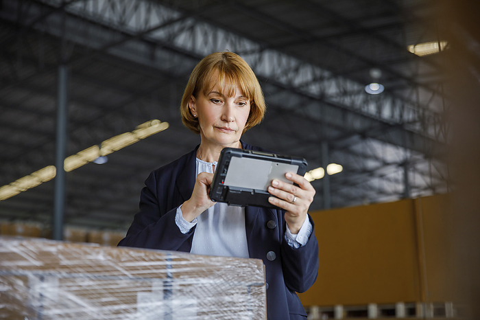 Manager using tablet PC standing by stocks in warehouse