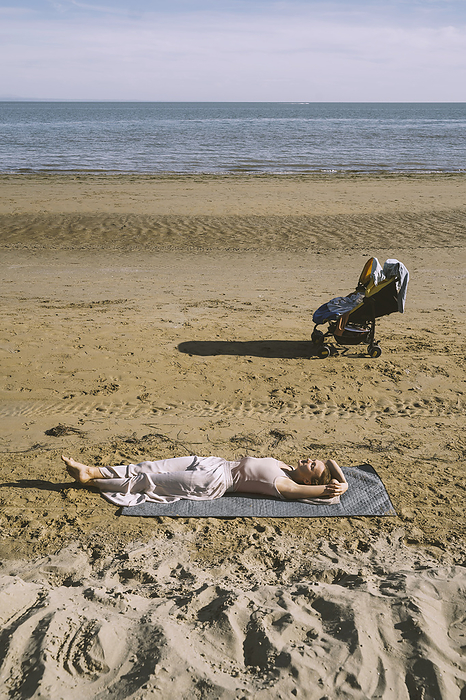 Mother lying on sand with son in stroller at beach